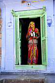 A colorful Rajasthani woman stands at the front door of her house, the house is a traditional colorful house