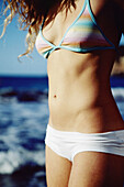 Body part of a woman in bikini by the sea