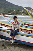 Boy sitting on a fishing boat, Playa El Tirano, Isla de Margarita, Nueva Esparta, Venezuela