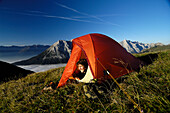 Junge Frau schaut aus einem Zelt in den Bergen, Tirol, Österreich, Europa
