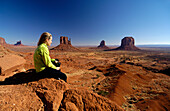 Junge Frau auf einem Fels sitzend betrachtet die Aussicht, Monument Valley, Utah, Nordamerika, Amerika