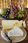 Brie and Emmanthaler (Swiss) on cheese cutting board with fruit and baguette.