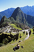 Machu Picchu Inca ruins, terraces, visitor sitting on terrace, and Huayna Picchu, Peru