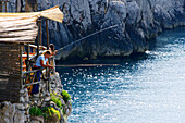 Menschen angeln an der Felsküste im Sonnenlicht, Capri, Italien, Europa