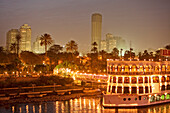 Illuminated ship on the Nile in front of palm trees and high rise buildings, Cairo, Egypt, Africa