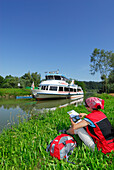 Woman sitting in meadow near river Danube while reading, Ardagger Markt, Lower Austria, Austria