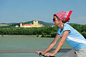 Female cyclist riding along Danube river, Melk abbey in background, Danube Cycle Route Passau to Vienna, Wachau, Lower Austria, Austria