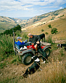 Schafzüchter Lou Thacker mit Sohn und Hütehunden vor weitem Weideland, Rowendale Homestead, Okains Bay, Banks Peninsula, Südinsel, Neuseeland