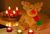Rudolph the Red-Nosed Reindeer as stuffed animal sitting in front of burning candles, with advent wreath in background
