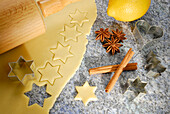 Stars cutted out of cookies dough, cookie cutters for Christmas cookies, rolling pin, lemon, cinnamon and star anise laying at worktop