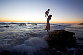 Mother and child on a rock on the waterfront at sunset, Punta Conejo, Baja California Sur, Mexico, America