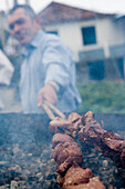 Mann grillt Espetada Rindfleisch Lorbeerspieße bei religiösem Fest, Ponta Delgada, Madeira, Portugal
