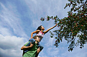 Woman on man's shoulders, reaching for an apple, Styria, Austria