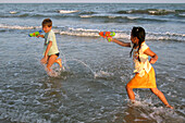 Children Playing With Water Pistols On The Edge Of The Beach