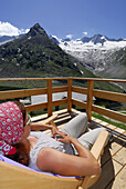 Woman sunbathing on terrace of hut Berliner Huette with view to Steinmandl and Grosser Moeseler, Zillertal, Zillertal Alps, Tyrol, Austria
