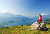 Frau sitzt auf einem Felsblock und blickt auf Comer See, Monti Lariani, Lombardei, Italien