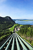 Fallrohre des Wasserkraftwerks Walchensee und Hochspannungsmasten, Kochelsee im Hintergrund, Bayerische Alpen, Oberbayern, Bayern, Deutschland