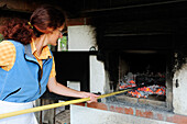 Woman removing burning charcoal from oven, Upper Bavaria, Bavaria, Germany