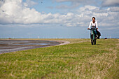 Radfahrerin auf einem Deich, Beltringharder Koog, Lüttmoorsiel, Nordstrand, Schleswig-Holstein, Deutschland