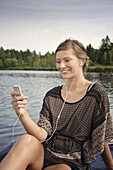 Young woman listening to music while sitting on a jetty at lake Starnberg, Bavaria, Germany