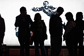 Silhoutte of group of people waiting at a tram station with neon lit advertising behind them,  Hong Kong,  China,  East Asia