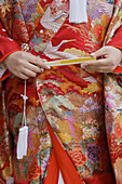 A close-up of the front of a Japanese bride´s wedding kimono,  showing her holding a closed fan in her hands in Shimogamo jinja in Kyoto