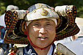 A head shot of a smiling Japanese man dressed up as a samurai for the Jidai Matsuri Festival of Ages in Kyoto,  showing showing helmet and head gear