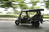 Tuk Tuk speeding past a park Bangkok,  Thailand