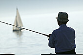 Fisherman at Lake Constance, sailing boat in the background, Lake Constance, Baden-Wuerttemberg, Germany
