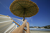 Womans' legs on a hammock under a thatched sun shade, Mallorca, Balearic Islands, Spain