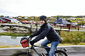 Junge Frau fährt mit dem Fahrrad und lächelt in die Kamera, Reine, Südlofoten, Lofoten, Nordnorwegen, Norwegen, Skandinavien, Europa