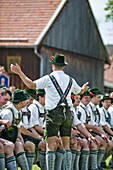 Young men wearing traditional costumes sitting side by side, May Running, Antdorf, Upper Bavaria, Germany