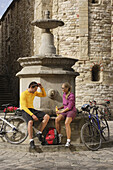 Young couple with bicycles resting at the fountain of San Leo, Marche, Italy, Europe