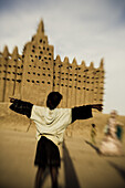 Girl with open arms in front of the Mosque of Djenna, Mali, Africa