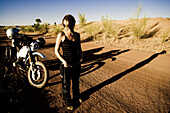 Young woman and motorcycle on dirt road in the evening sun, Mali, Africa