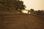 Man on motorcycle riding on a dirt road in the evening, Mali, Africa