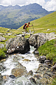 Female hiker passing a stream, valley Val da Natons, Canton of Grisons, Switzerland