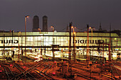 Schienen und Bahnhofsgebäude, beleuchtet, Frauenkirche im Hintergrund, Hauptbahnhof München, München, Oberbayern, Bayern, Deutschland