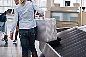 Woman taking suitcase off a baggage conveyor belt, Munich airport, Bavaria, Germany