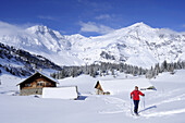 Female backcountry skier near alpine huts, Hoher Sonnblick and Hocharn in background, Rauris valley, Goldberg mountain range, Hohe Tauern, Salzburg, Austria