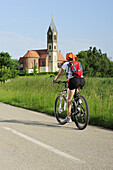 Fahrradfahrerin, Kirche St. Laurentius im Hintergrund, Großenried, Bechhofen, Altmühltal-Radweg, Bayern, Deutschland