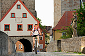 Female cyclist passing bridge, town gate in background, Ornbau, Altmuehltal cycle trail, Bavaria, Germany
