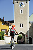 Woman cycling towards city gate, Kelheim, Altmuehltal cycle trail, Bavaria, Germany