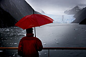 Mann mit rotem Regenschirm bestaunt den Garibaldi Gletscher von an Bord Kreuzfahrtschiff MS Deutschland (Reederei Deilmann), Chilenische Fjorde, Beagle Kanal, Patagonien, Chile, Südamerika, Amerika