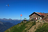 Segelflugzeug und Schweizer Flagge an der Berghütte Capanna Tamaro, Bergwanderung zum Monte Tamaro, Tessin, Schweiz