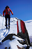 Rock with marker, woman backcountry skiing out of focus in the background, Staller Sattel, Villgratner Berge range, South Tyrol, Italy