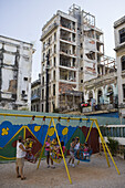 Kinder auf Schaukel an Spielplatz vor baufälligen Hochhäusern, Havanna, Kuba, Karibik