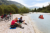 Cyclists resting at river Isar, Isar Cycle Route between Wallgau and Vorderriss, Karwendel range, Upper Bavaria, Germany