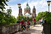 Cyclists passing Kabelsteg bridge, St. Luke's Church in background, Isar Cycle Route, Munich, Upper Bavaria, Germany