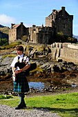 Great Britain, Scotland, Dornie, Bagpiper and castle of Eilean Donan